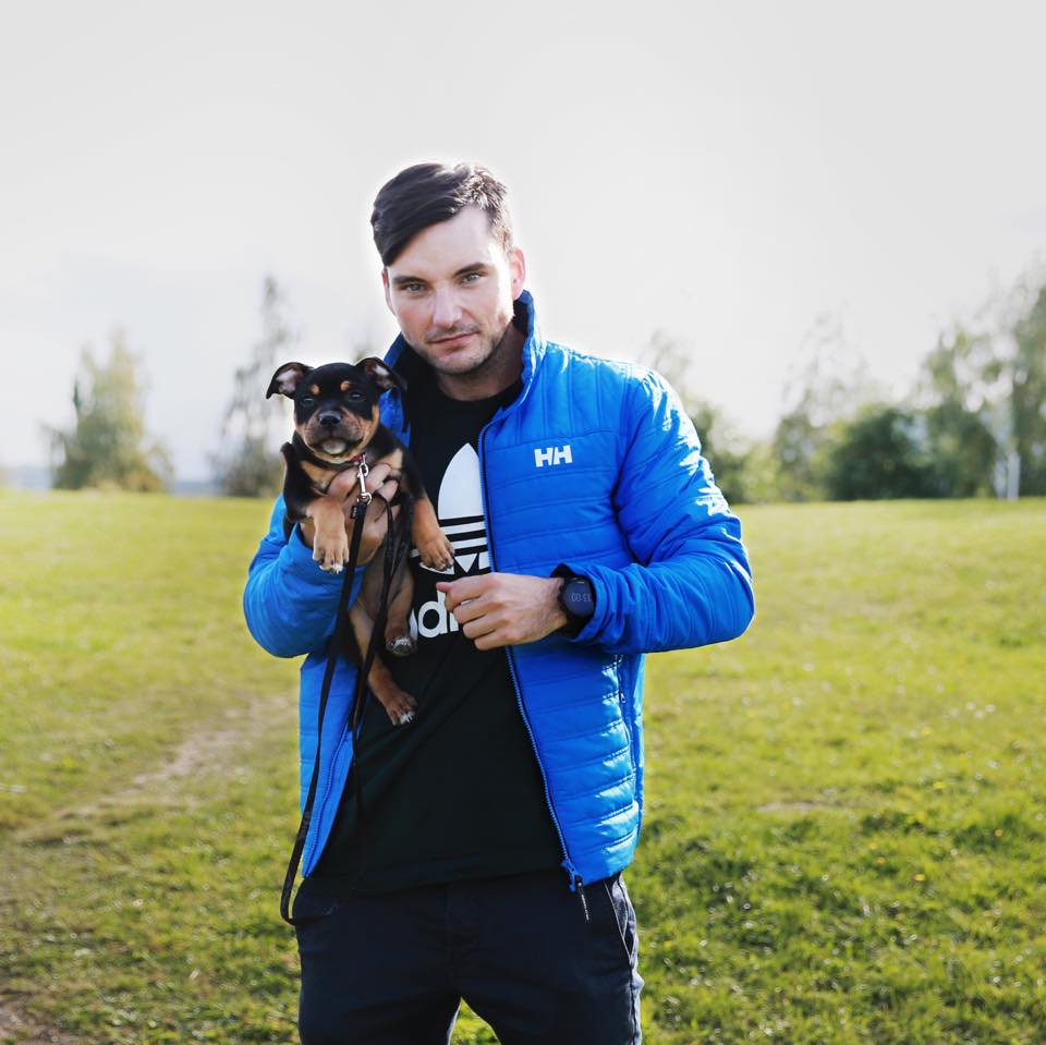 Fredrik holding his dog in a green field.